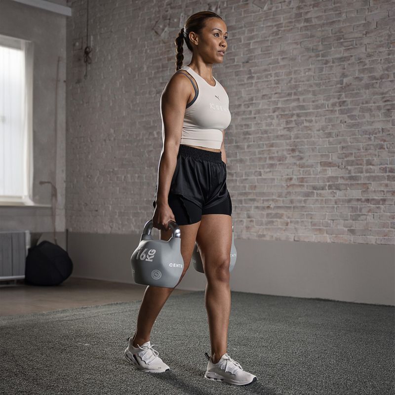 Frau hält in jeder Hand eine 16 kg Kettlebell und macht die HYROX-Übung Farmer's Carry