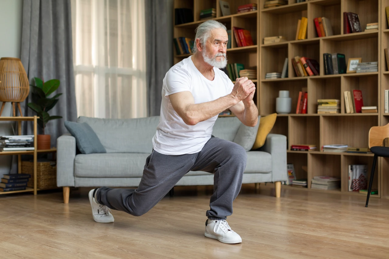 Senior trainiert Ausfallschritte aka. Lunges im Wohnzimmer zur Verbesserung seiner Balance